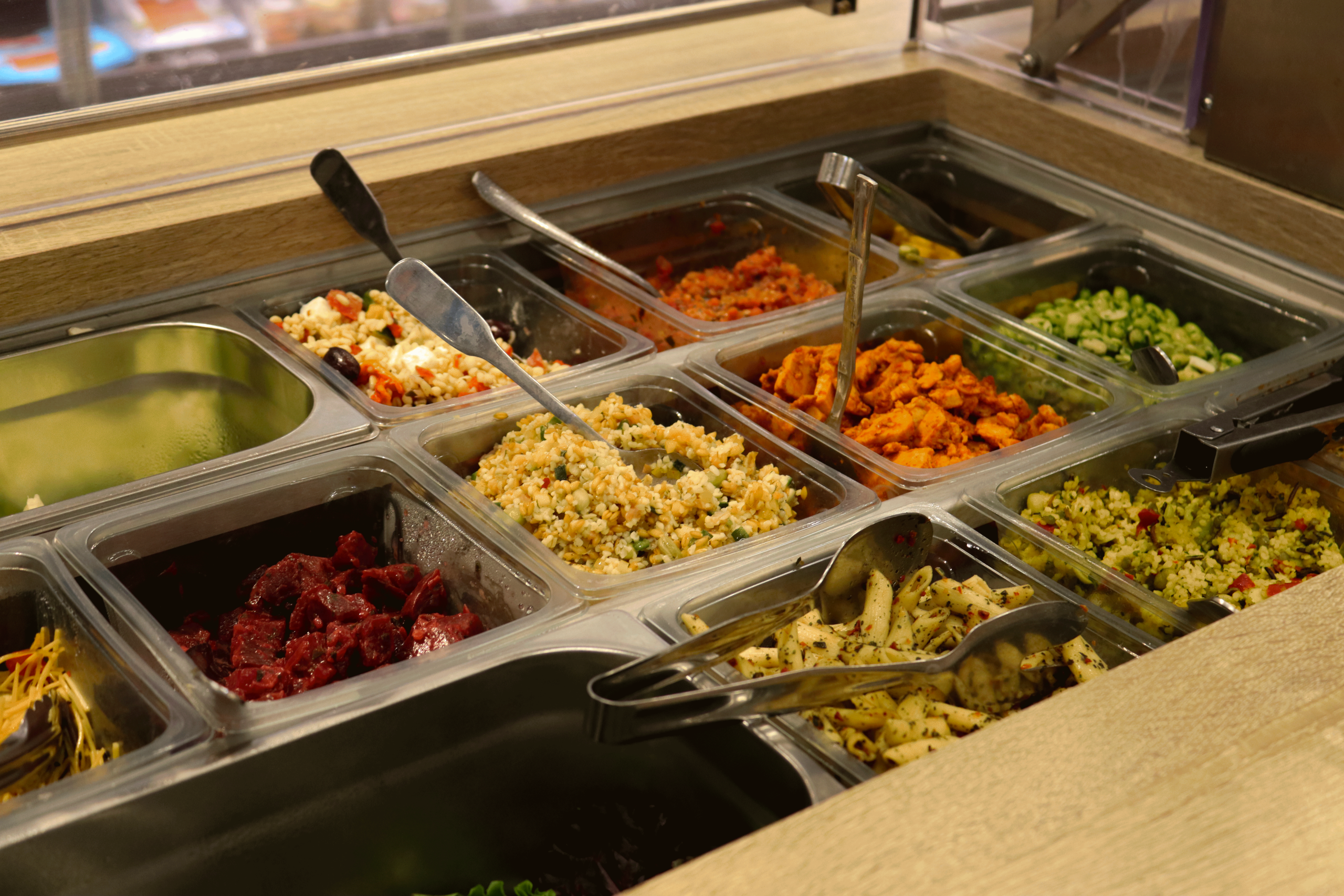 Photos d'un bar à salade avec des préparations tels que des salades de pâtes, du poulet aux épices etc...